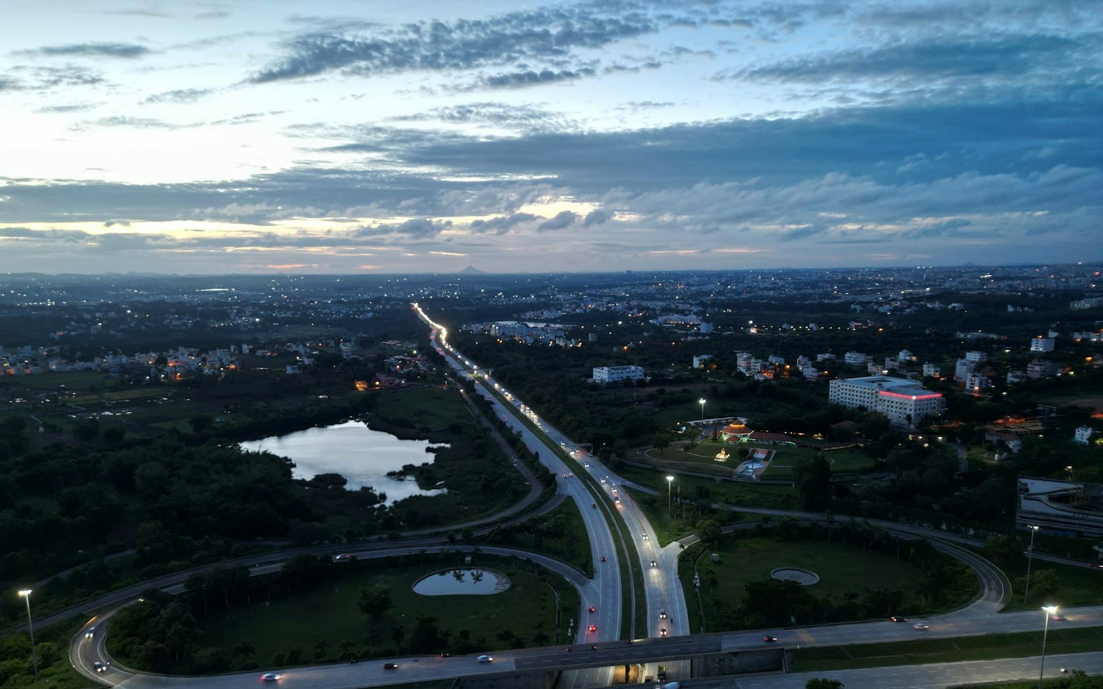 Aerial view of a highway interchange at dusk, with vehicle headlights streaming towards the city