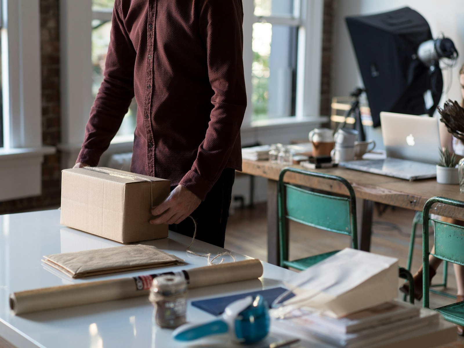 Person packing an e-commerce order, tying twine around a cardboard box beside kraft paper and a tape dispenser